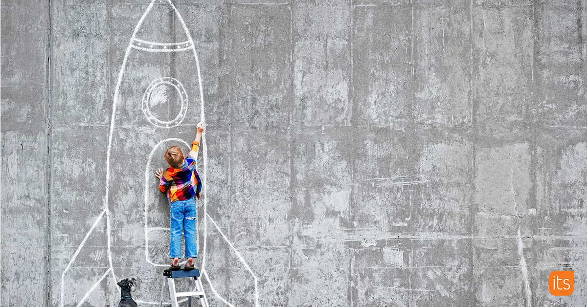 Foto av en elev som står foran en betongvegg med en krittpinne i hånden og tegner en rakett.